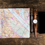 Sebuah map, handphone, jam tangan, dan bolpoin di atas meja kayu